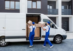 Two removal company workers unloading boxes from minibus into new home.